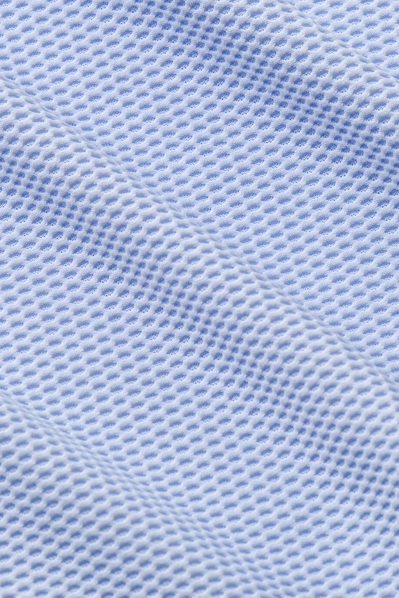 Close-up of Twillory's AIR Zip Polo Solid in Powder Blue, featuring 360° Airflow Fabric with a textured grid pattern. Small, evenly spaced holes enhance breathability, and diagonal folds highlight the soft material's unique weave.