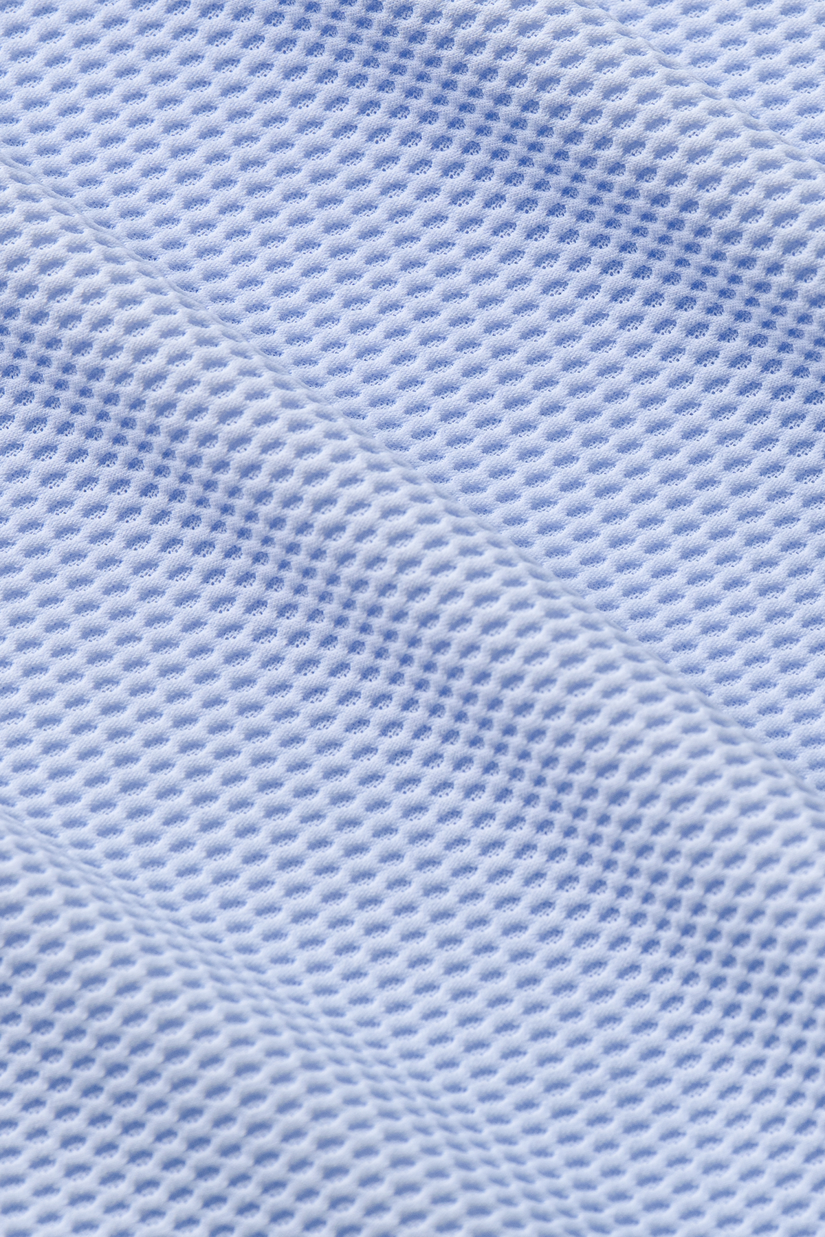 Close-up of Twillory's AIR Zip Polo Solid in Powder Blue, featuring 360° Airflow Fabric with a textured grid pattern. Small, evenly spaced holes enhance breathability, and diagonal folds highlight the soft material's unique weave.