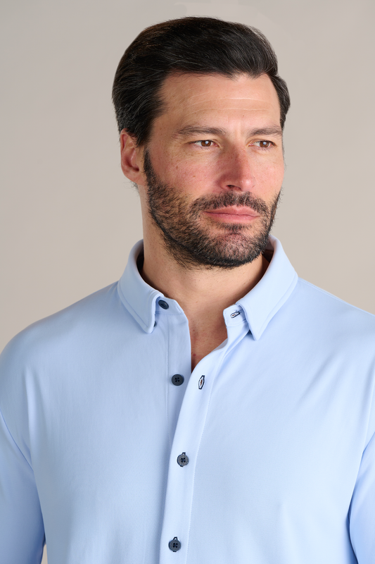 A man with short dark hair and a trimmed beard wears the Twillory Long Sleeve Button Down Polo Contrast in Powder Blue Navy, featuring dark buttons. He looks slightly right with a neutral expression against a plain light beige background.