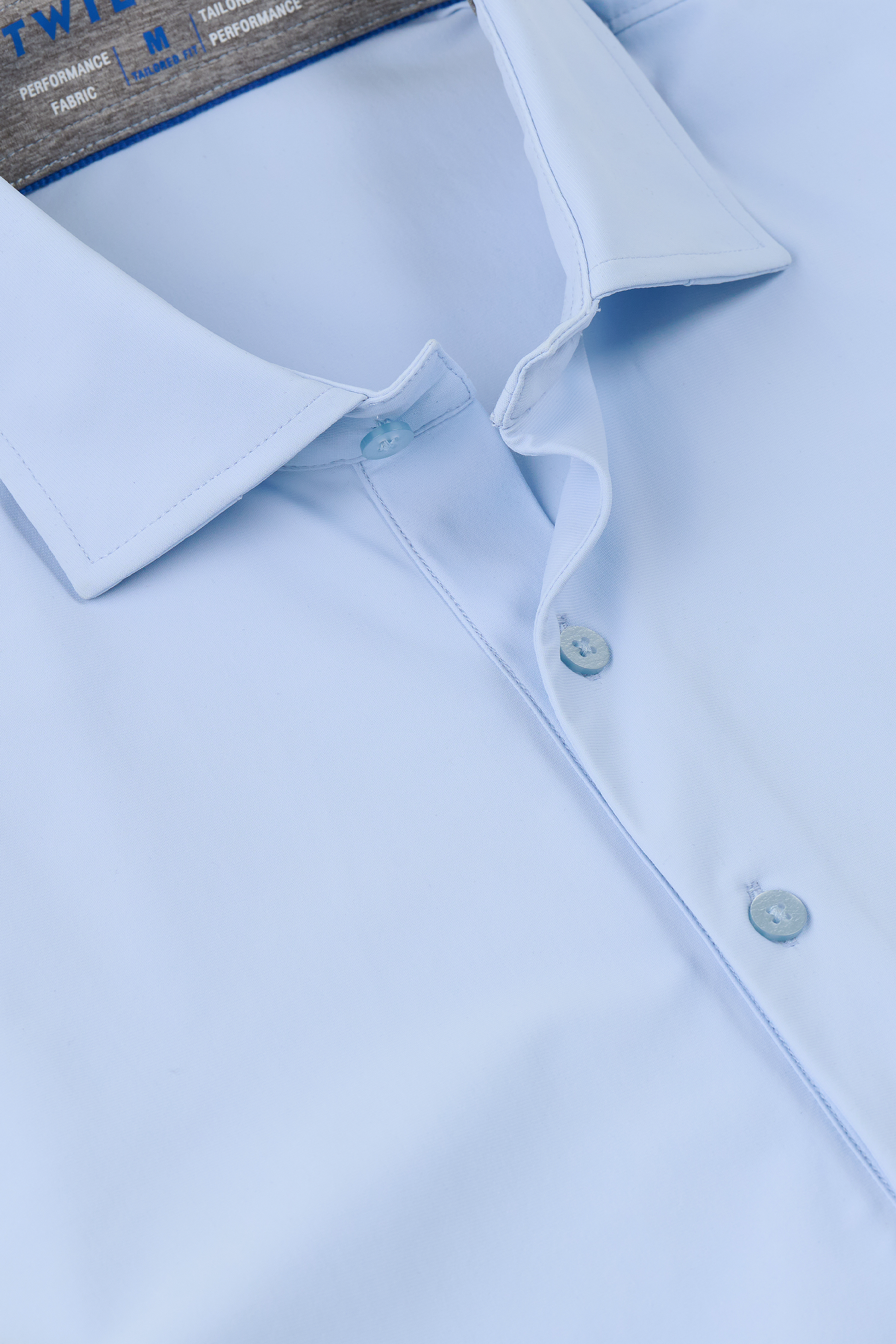 A close-up of the Twillory Event Polo Solid in Powder Blue on a hanger highlights its crisp collar, three buttons, smooth wrinkle-free fabric, and a glimpse of the shirt’s label at the top.