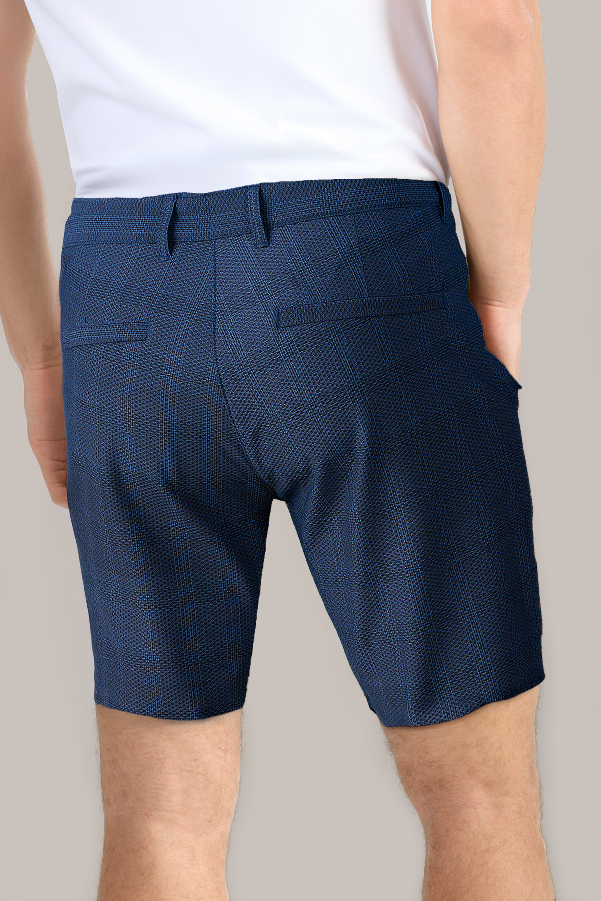 Someone wearing a white shirt and Twillory AIR Shorts in textured navy blue is seen from the back. The shorts feature sweat-wicking 360° Airflow Fabric, belt loops, side pockets, and two rear welt pockets against a light beige background.