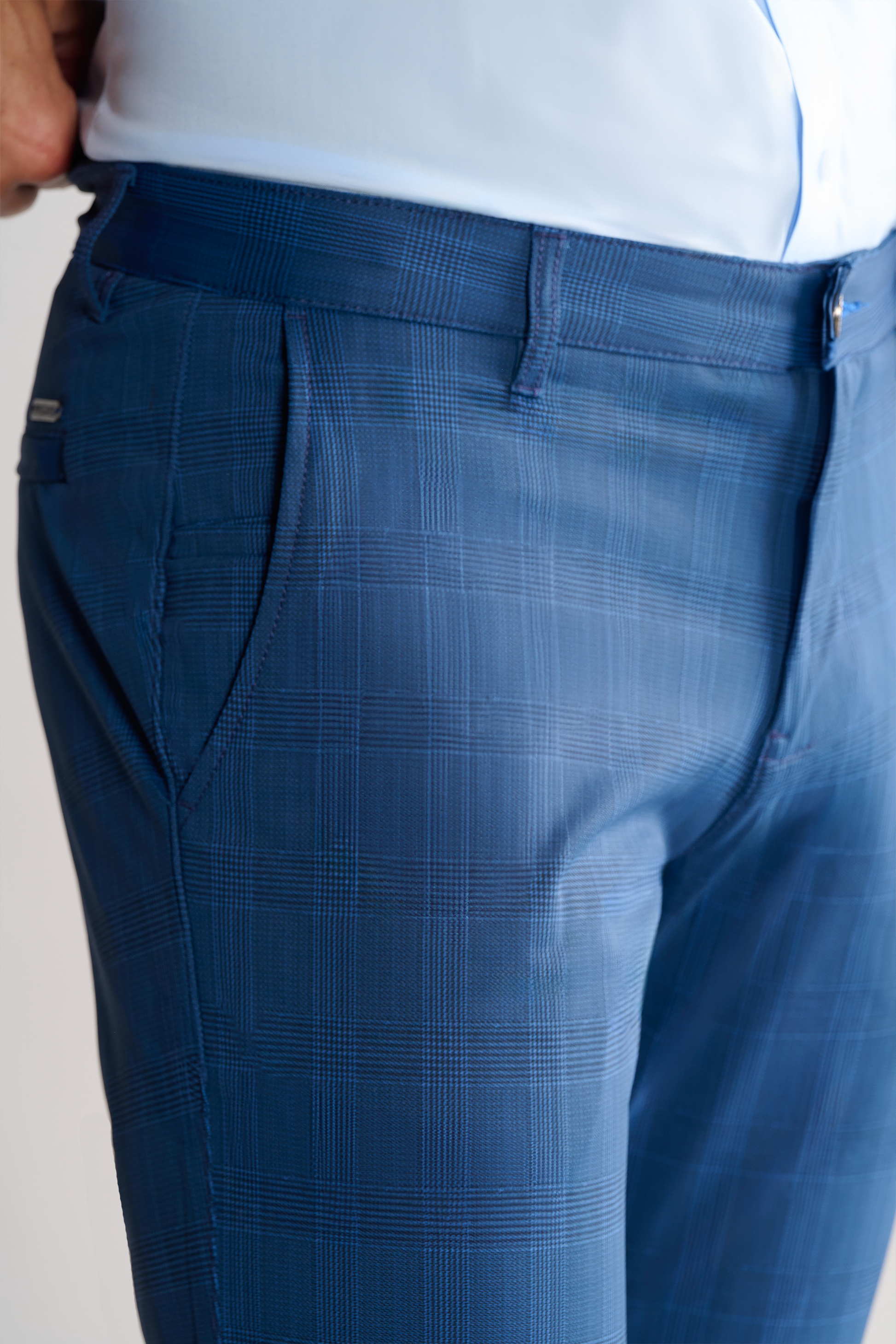 Close-up of a lower torso wearing Twillory Performance Pants // BLUE PRINCE OF WALES with front pockets, belt loops, shirt-gripping waistband, and subtle check pattern. Paired with a tucked-in light blue shirt; plain background.