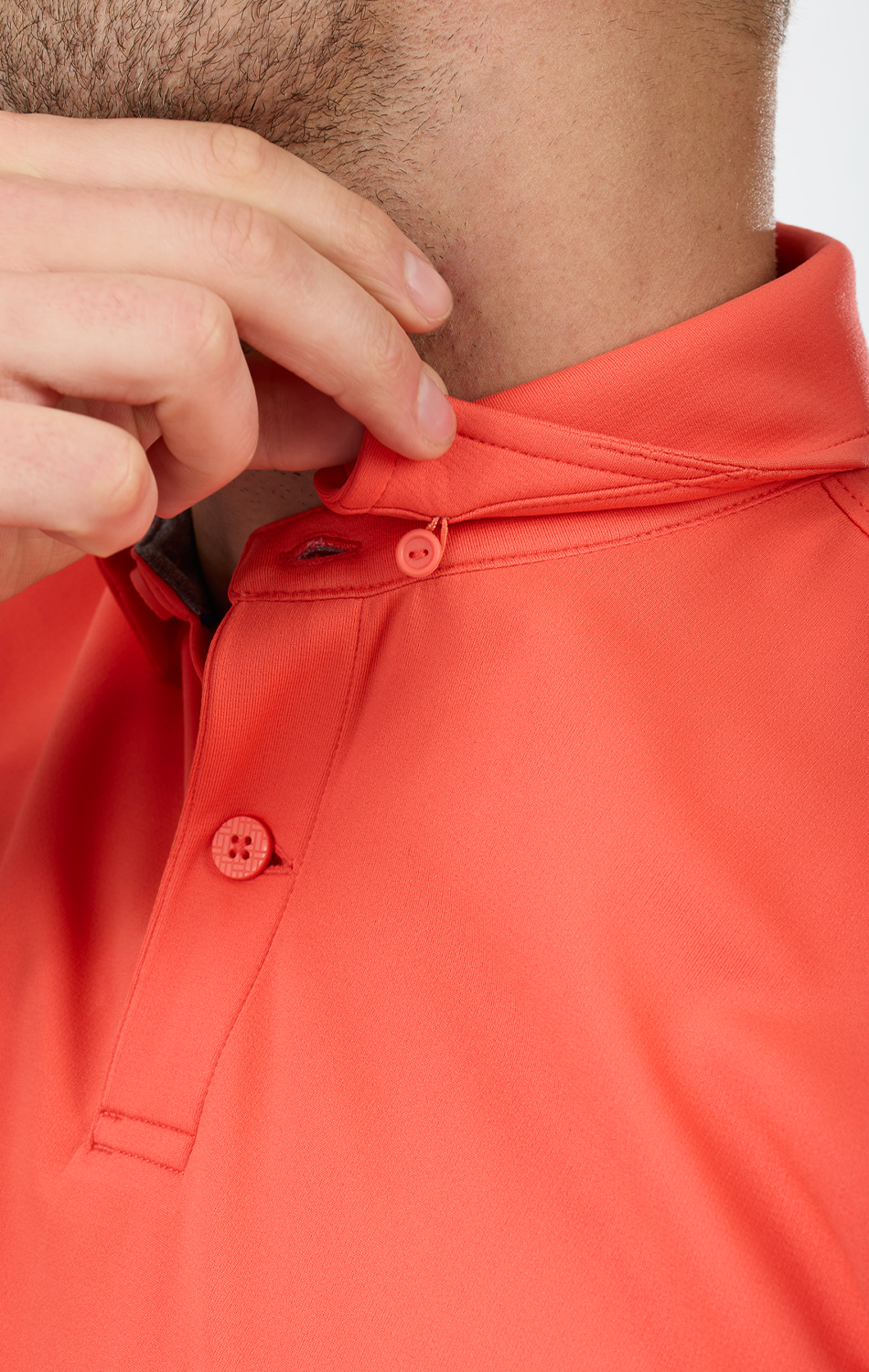A person in a Twillory Short Sleeve Polo Solid // Salmon fastens the top button near the collar, with only the lower face, neck, and hand visible. The tailored fit showcases smooth fabric and a subtle stitched detail by the collar.