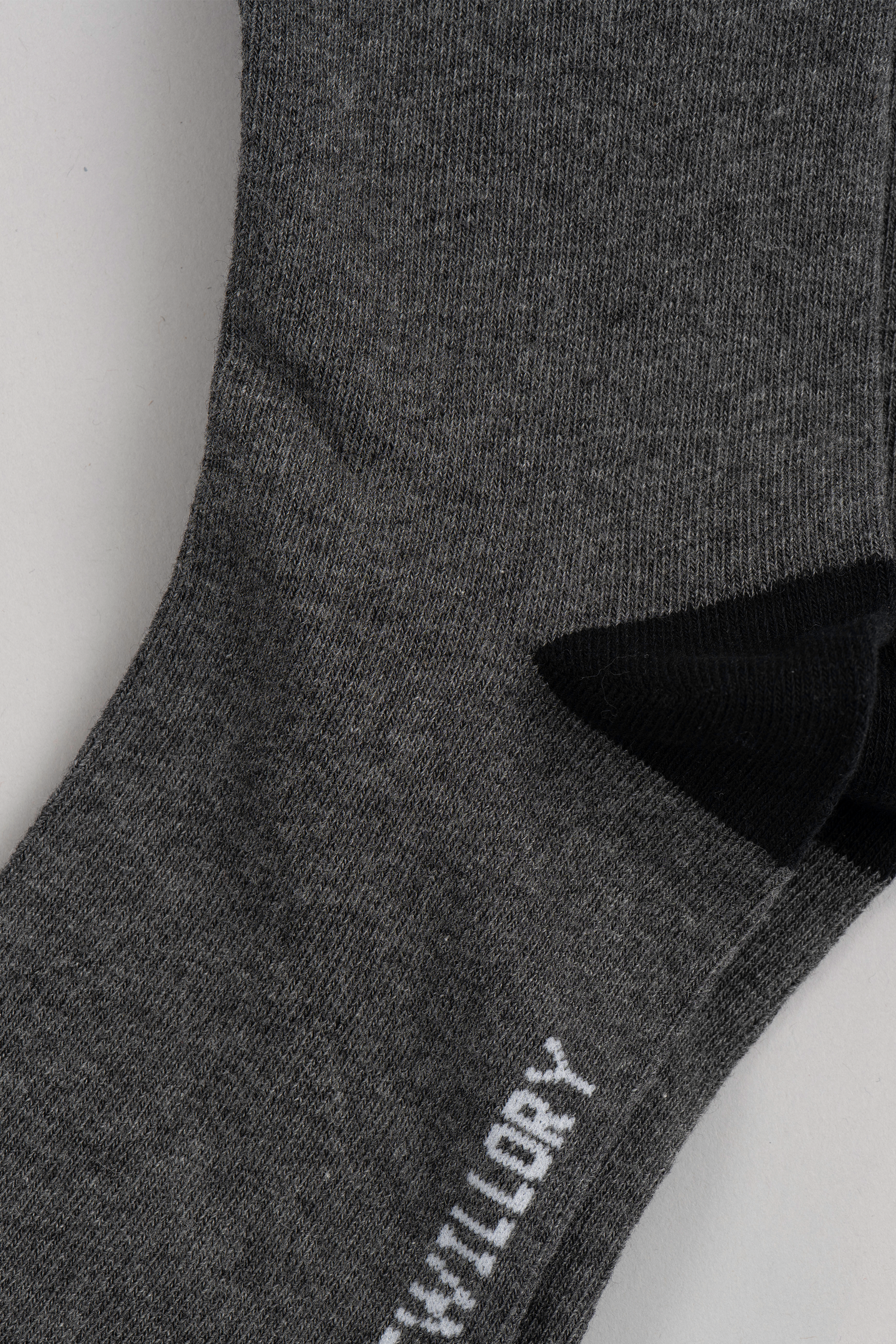 Close-up of a Twillory Grey Solid sock with a black heel, lying flat. Part of a white word is visible near the toe, while most text is cropped out. The soft, textured fabric makes these socks perfect for everyday comfort.