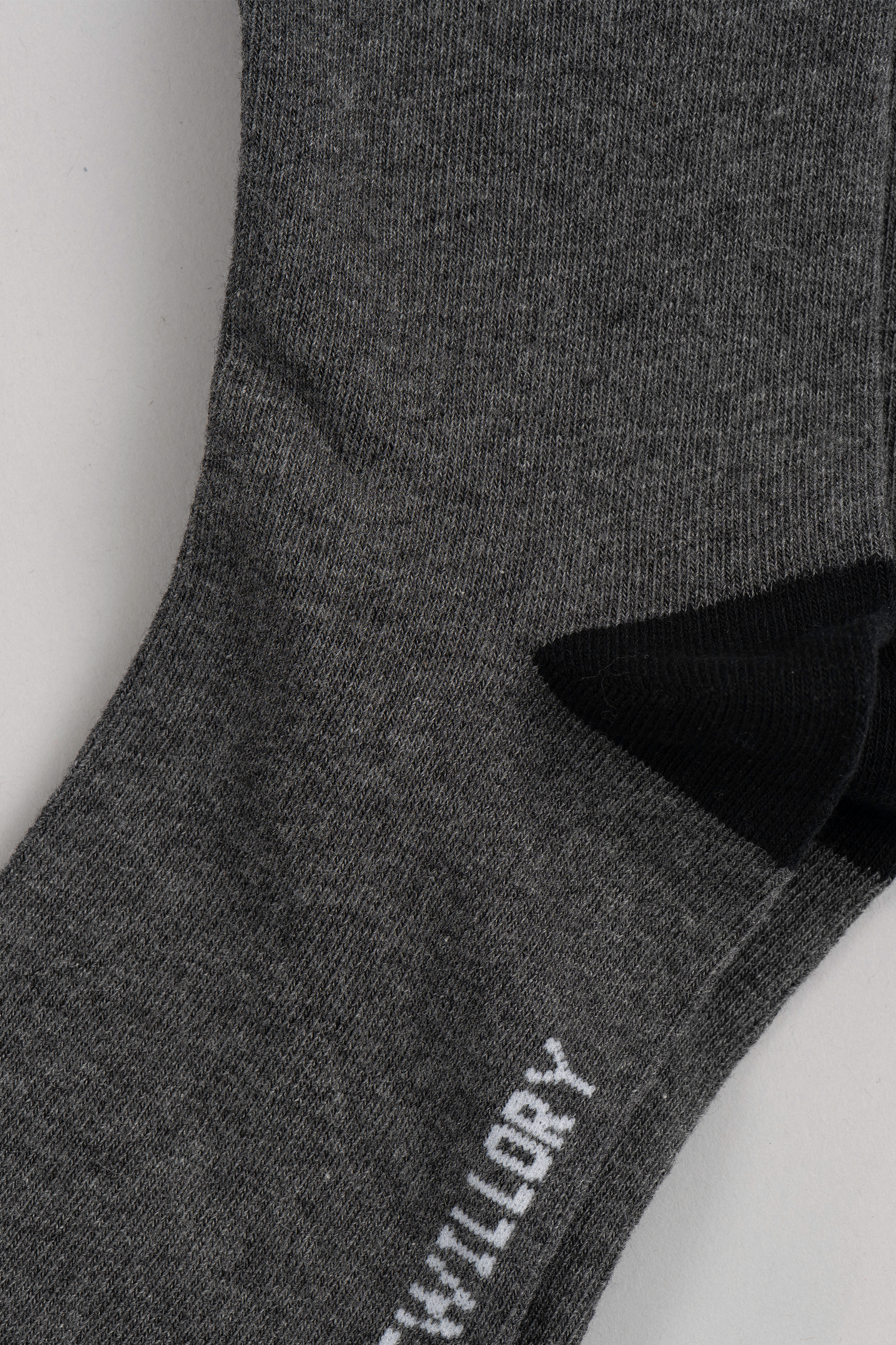 Close-up of a Twillory Grey Solid sock with a black heel, lying flat. Part of a white word is visible near the toe, while most text is cropped out. The soft, textured fabric makes these socks perfect for everyday comfort.