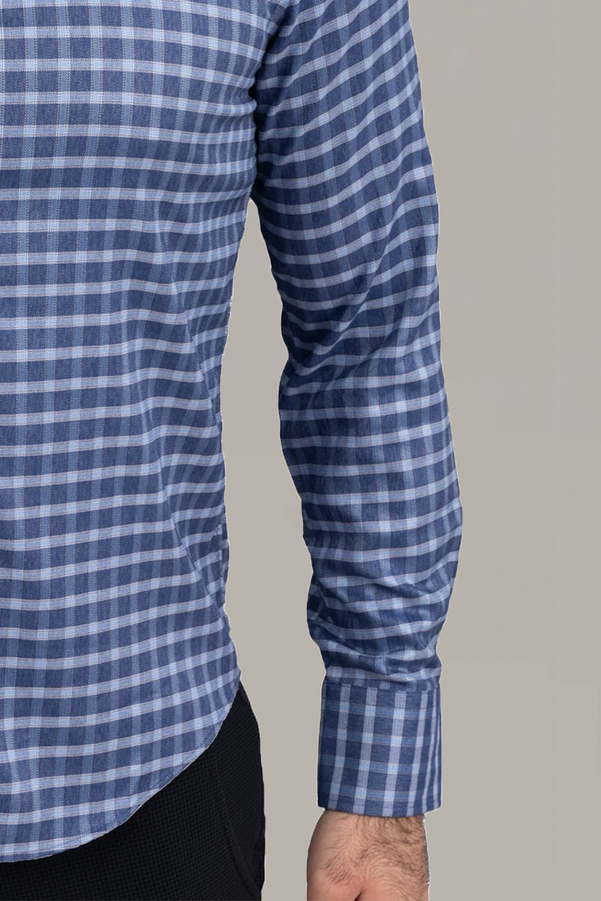 A person wears the Twillory untuck(able) Denim Windowpane shirt with black pants. Only their torso and right arm are shown, hand relaxed by their side, and the smart casual buttoned shirt is in focus against a plain light gray background.