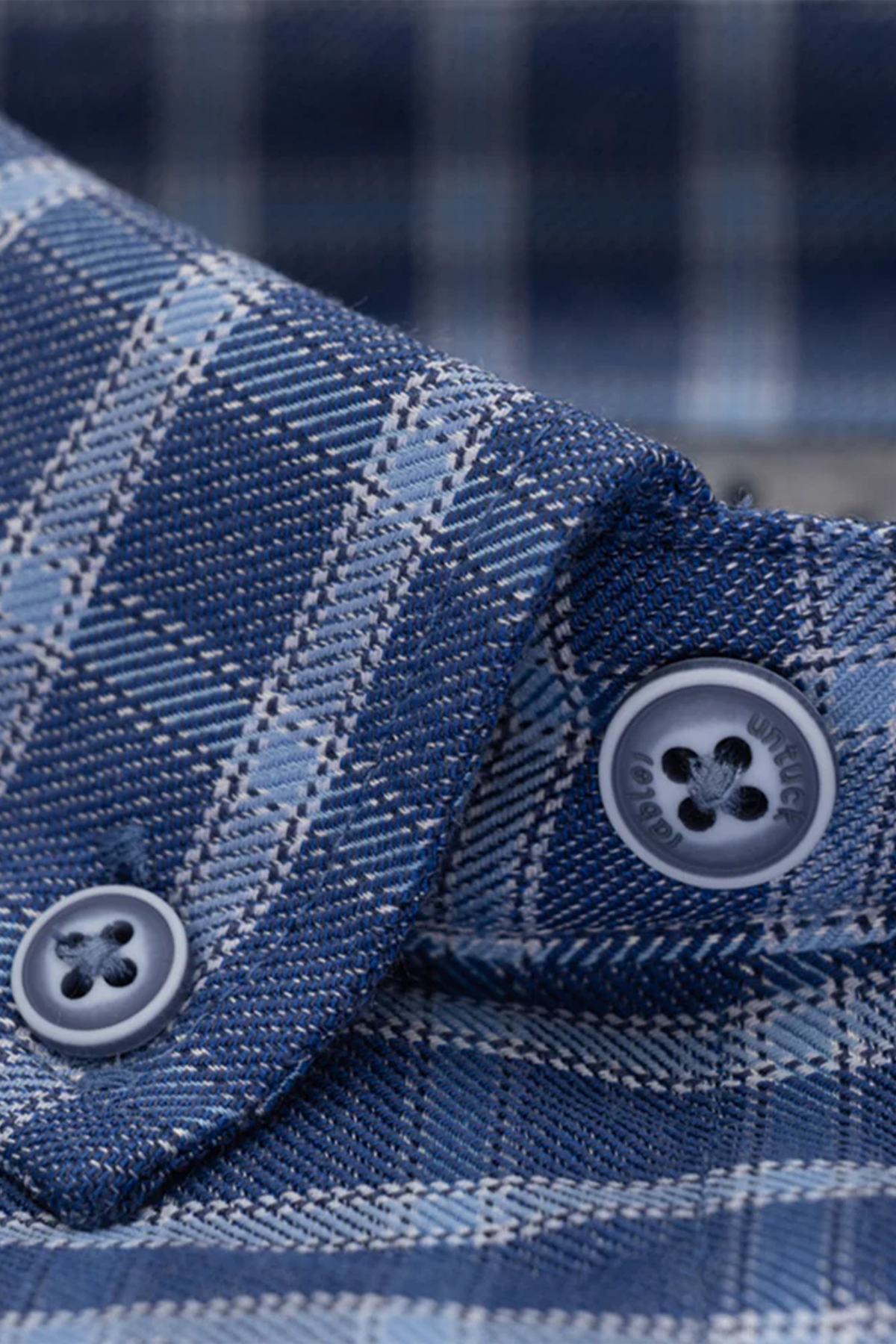 Close-up of the Twillory untuck(able) Denim Windowpane shirt collar with blue buttons. This smart casual shirt features intersecting light and dark blue windowpane checks, detailed stitching, and non-iron stretch fabric for comfort.