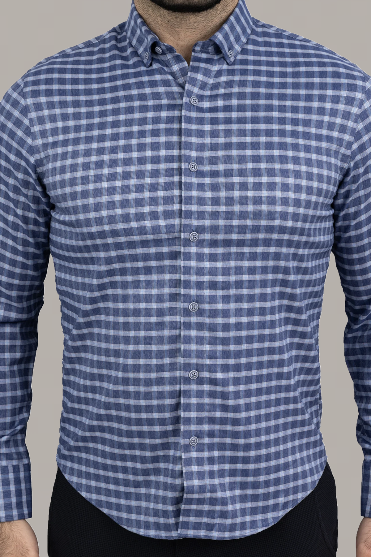 A man wears the Twillory untuck(able) Denim Windowpane shirt—a smart casual, long-sleeve button-up with a blue and white plaid pattern, button-down collar, and non-iron stretch fabric—shown against a plain light grey background.