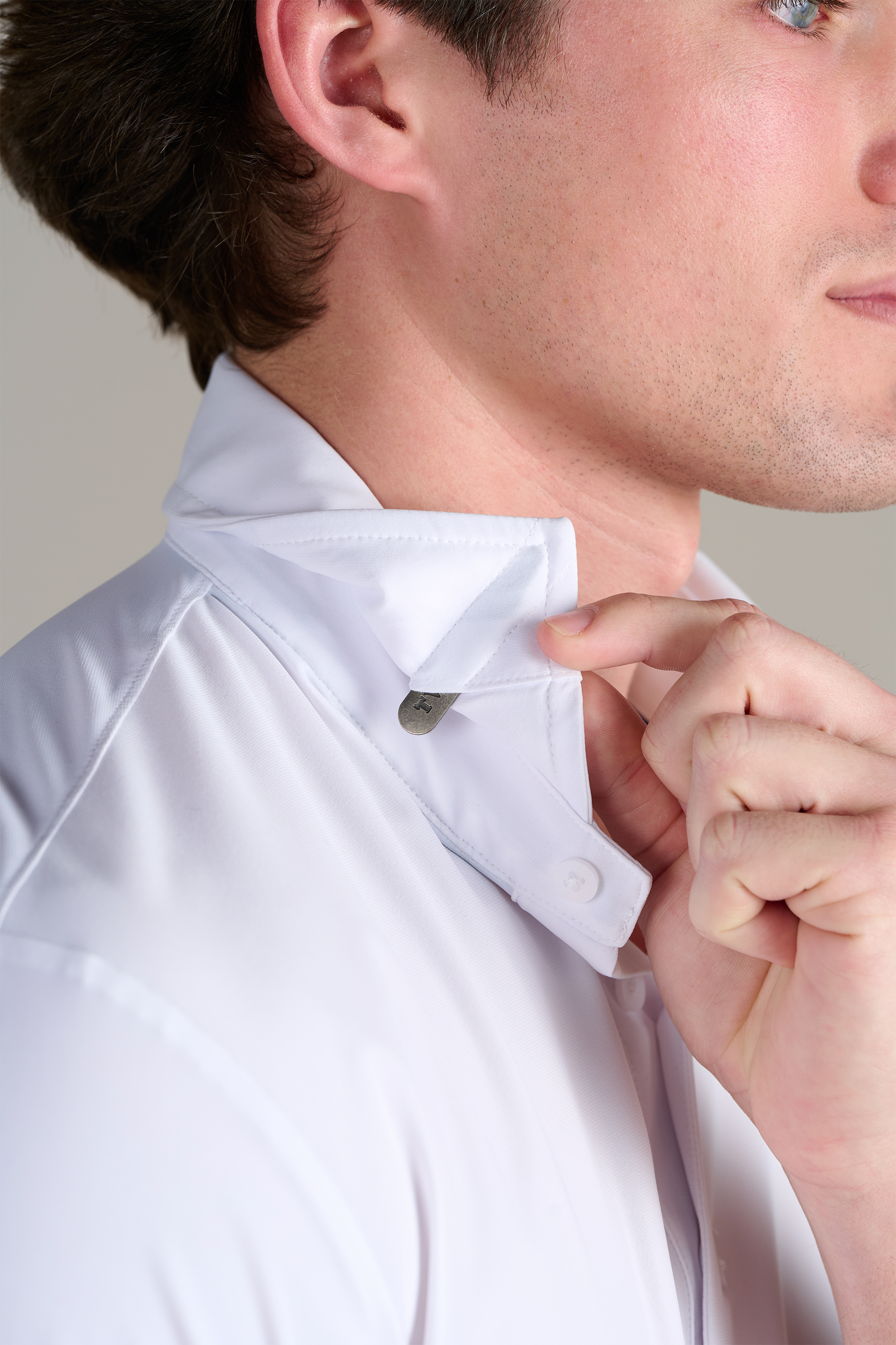 A person wearing Twillory’s Event Polo Solid in White lifts the collar with their right hand, revealing a hidden button detail. The wrinkle-free fabric and lower face are shown, highlighting the shirt's innovative design.