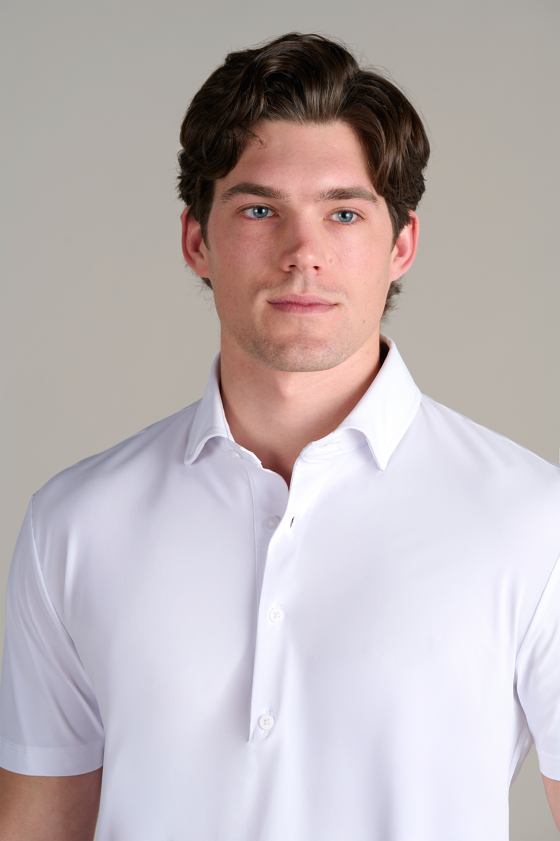 A young man with light skin and short brown hair wears the Twillory Event Polo Solid in white, facing forward with a neutral expression against a simple light gray background.