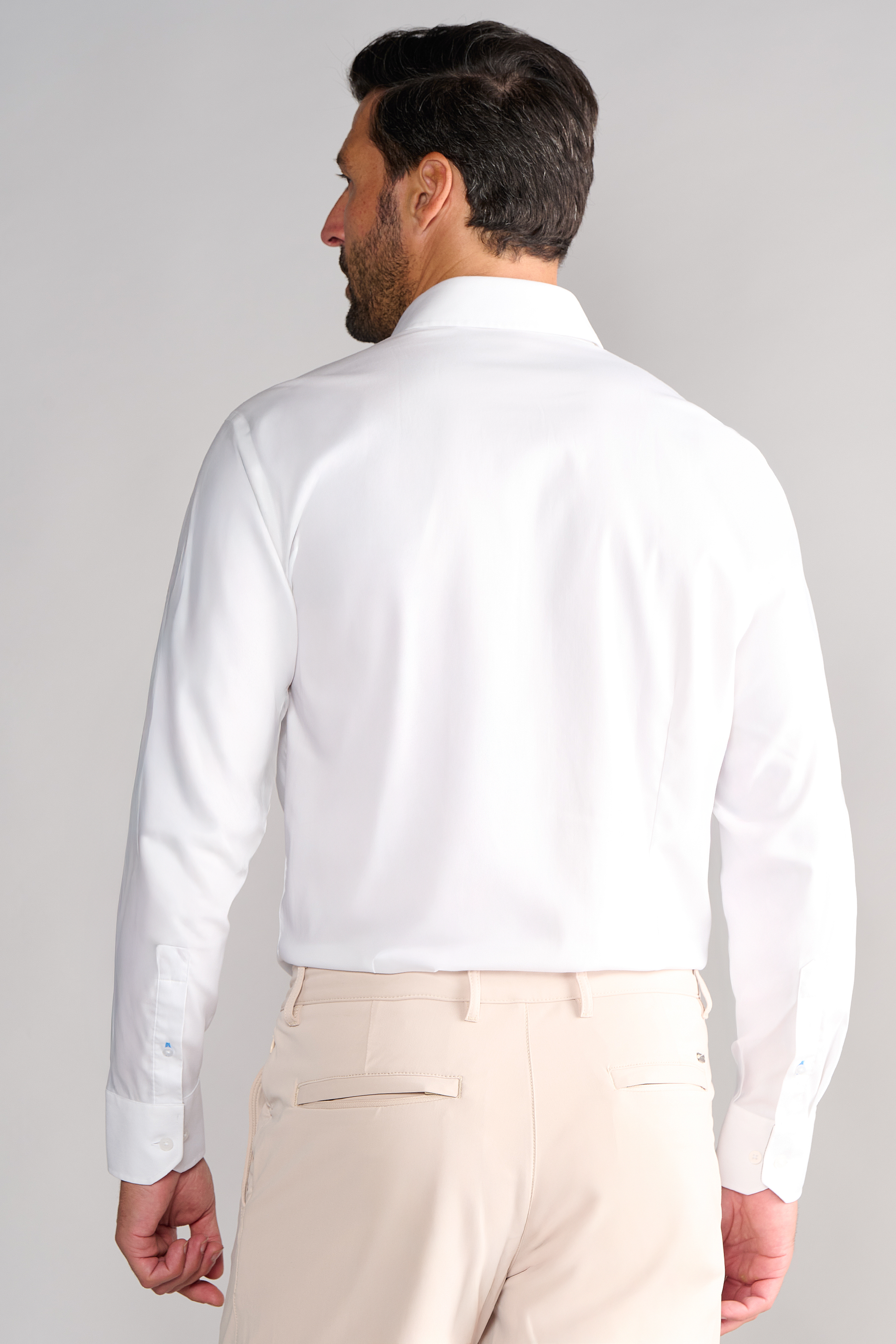 A man with short dark hair wears the Leader Solid // White non-iron dress shirt and beige pants, standing with his back to a plain light background.