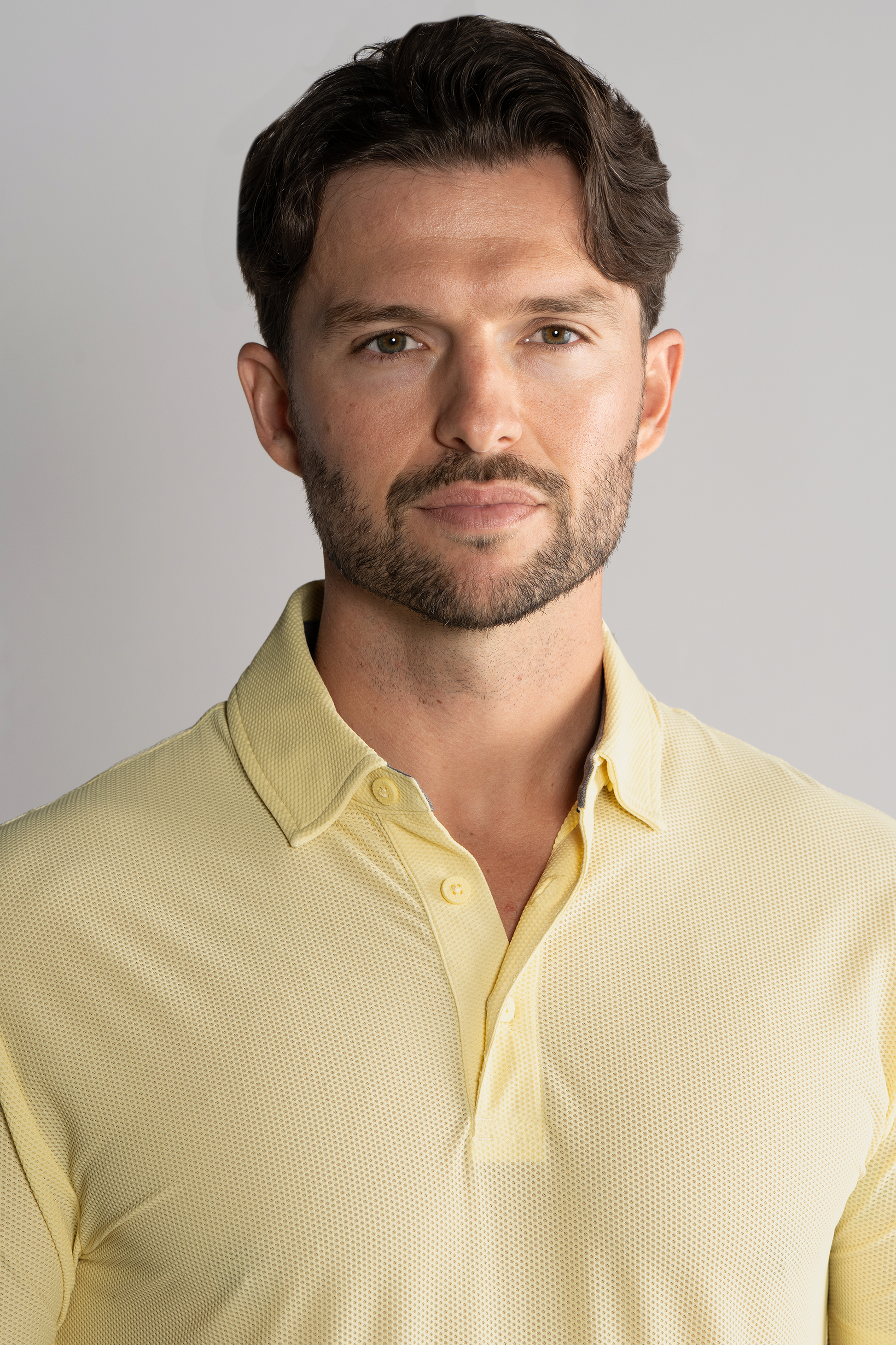 A man with short brown hair and a neat beard wears the Twillory AIR 3 Button Polo Solid in yellow. He faces the camera with a neutral expression against a plain, light gray background.