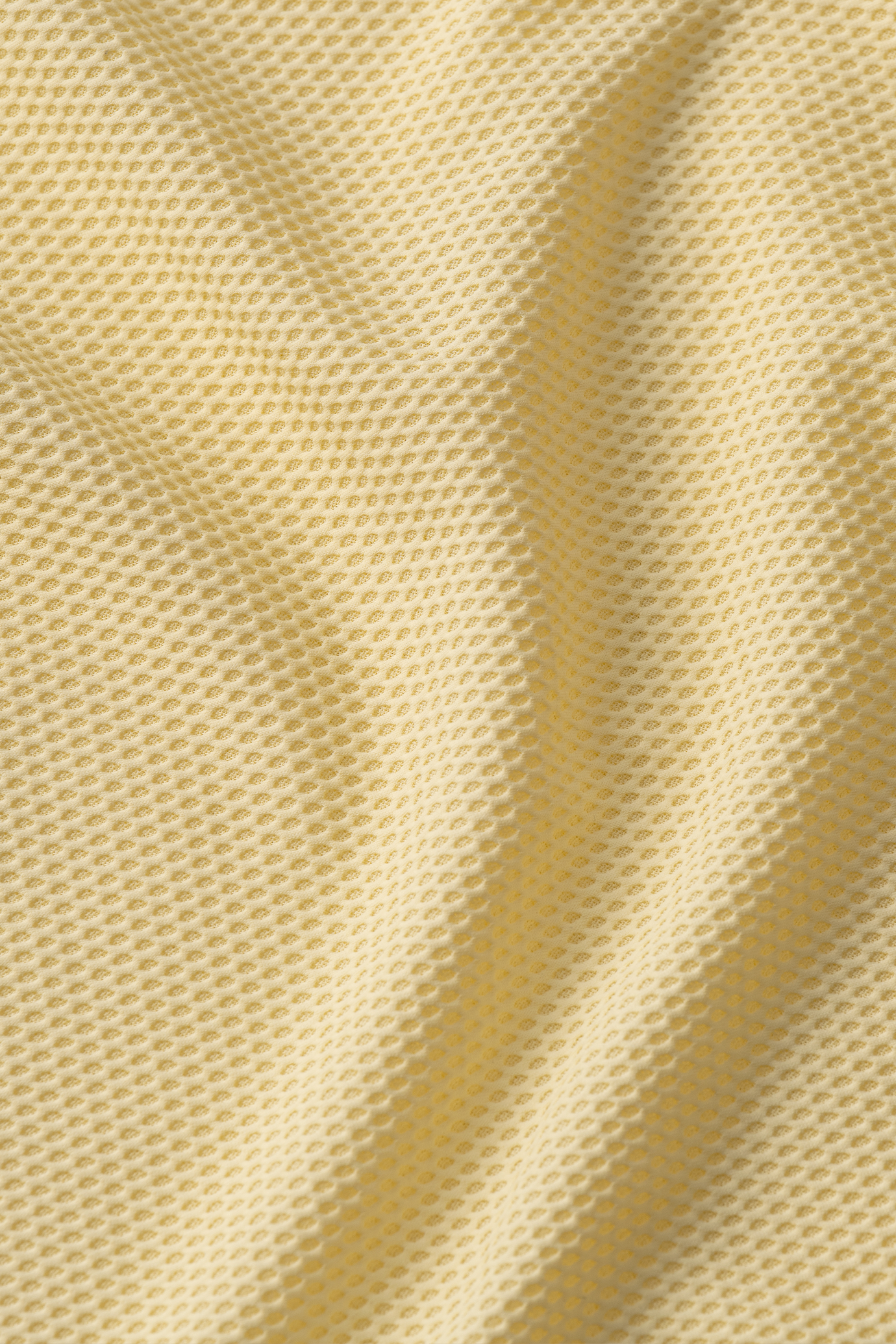 Close-up of Twillory's AIR Resort Shirt Solid in Yellow, made from cooling mesh fabric with a honeycomb pattern. Slight wrinkles create gentle curves and shadows, emphasizing its textured, hyper-breathable structure.