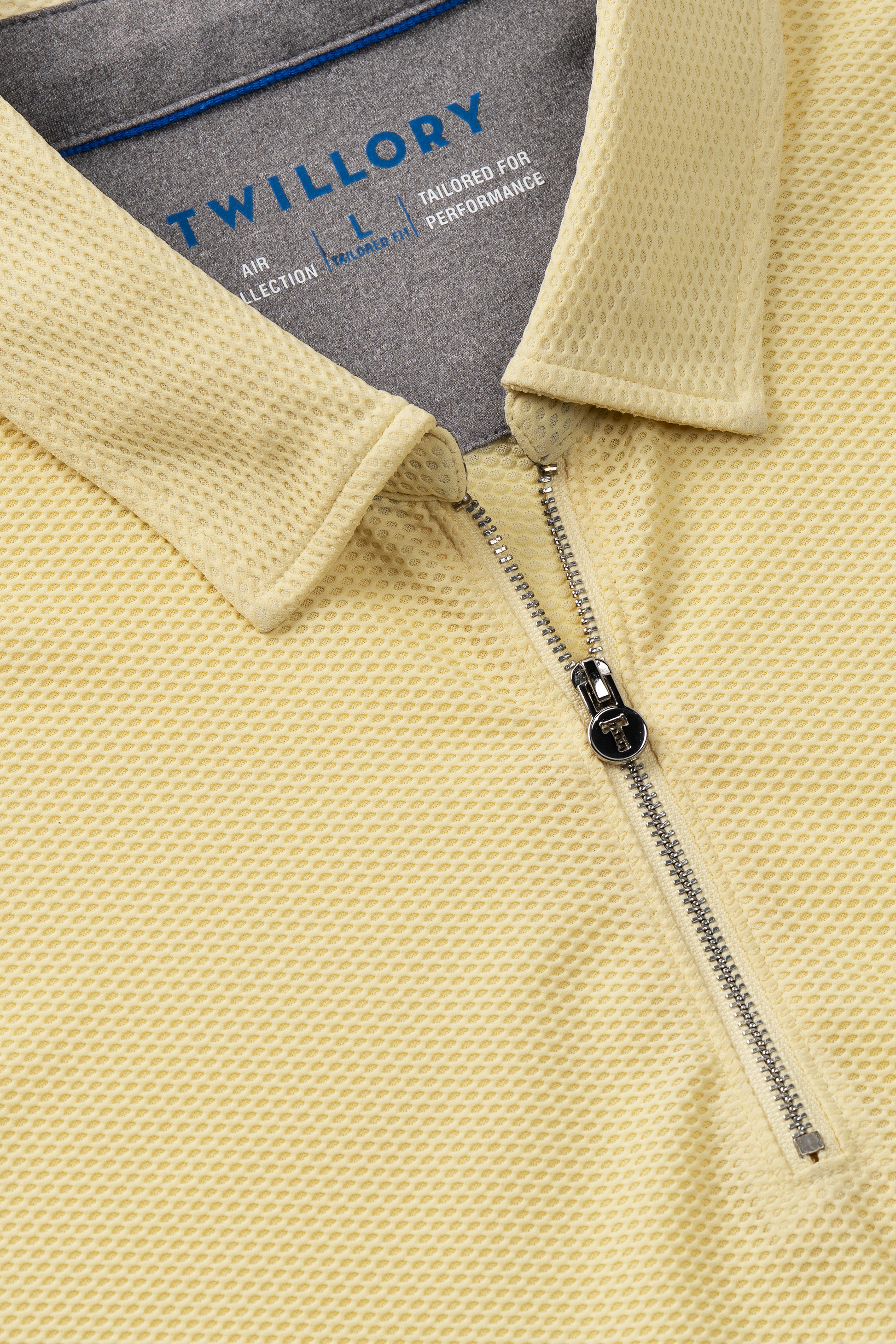 Close-up of the Twillory AIR Zip Polo Solid in yellow, featuring textured 360° Airflow mesh fabric, a silver half-zipper, folded collar, and gray lining with blue TWILLORY branding for enhanced breathability and style.