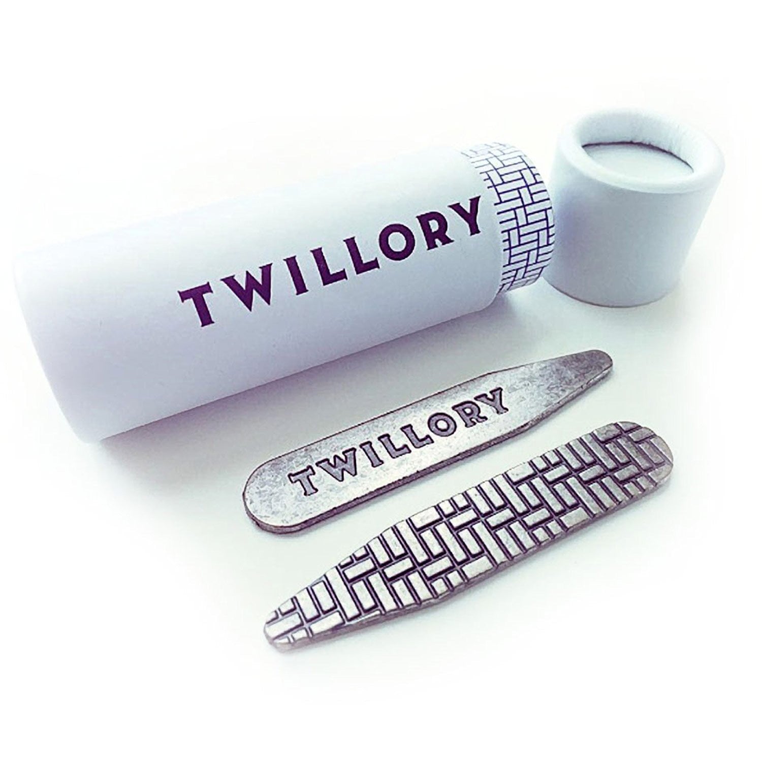 A white cylindrical Twillory container labeled "Collar Stays - 3 Pairs" sits beside two metal collar stays—one engraved with TWILLORY, the other sporting a matching basket-weave pattern found on the lid.