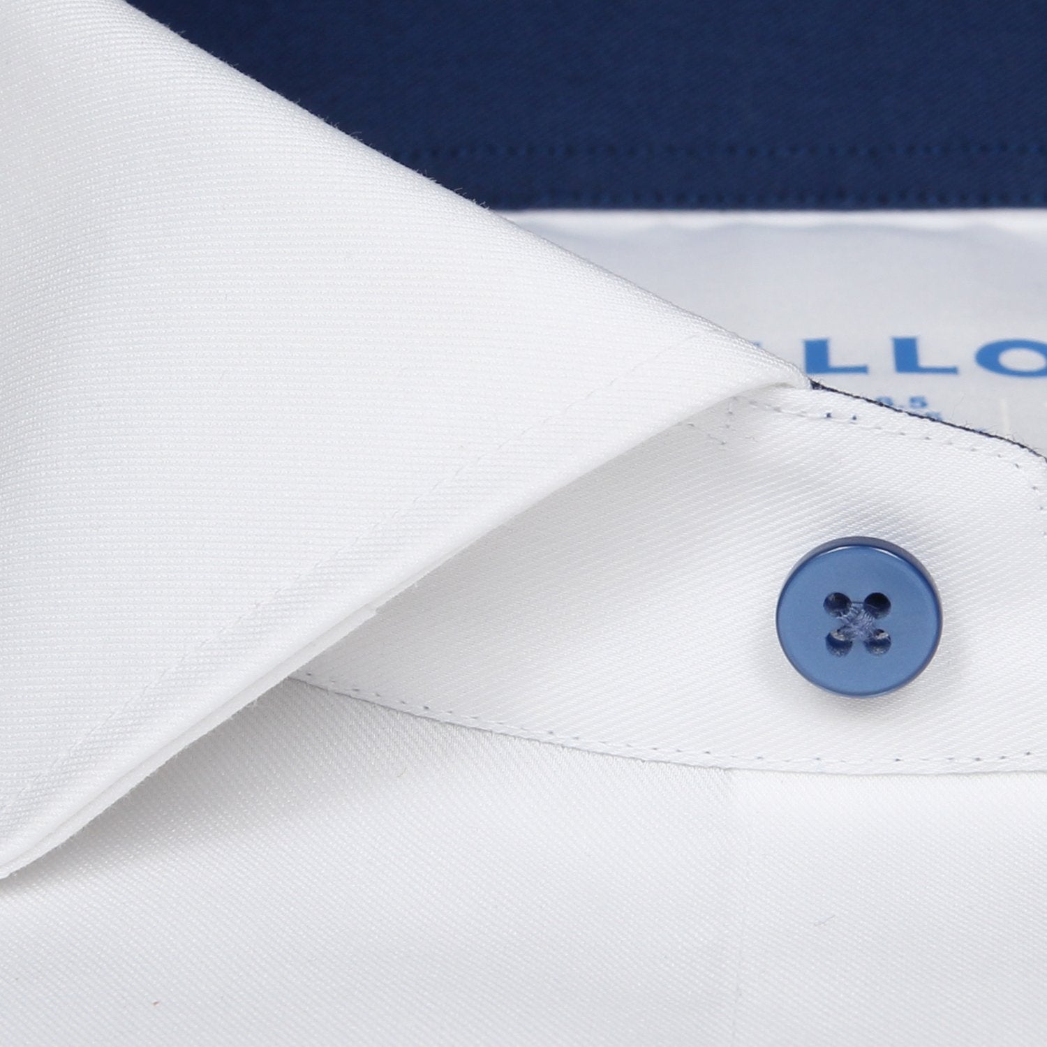 Close-up of the Twillory Leader Contrast // Navy shirt: a white collar with blue button, navy top, and visible stitching. Label with blue text below the collar. Features 4-way stretch and moisture-wicking fabric.