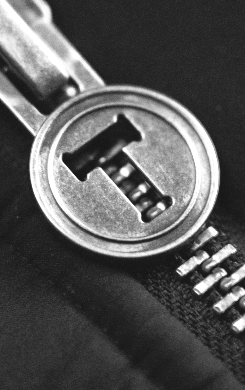 Close-up of a silver metal zipper pull on a dark fabric.
