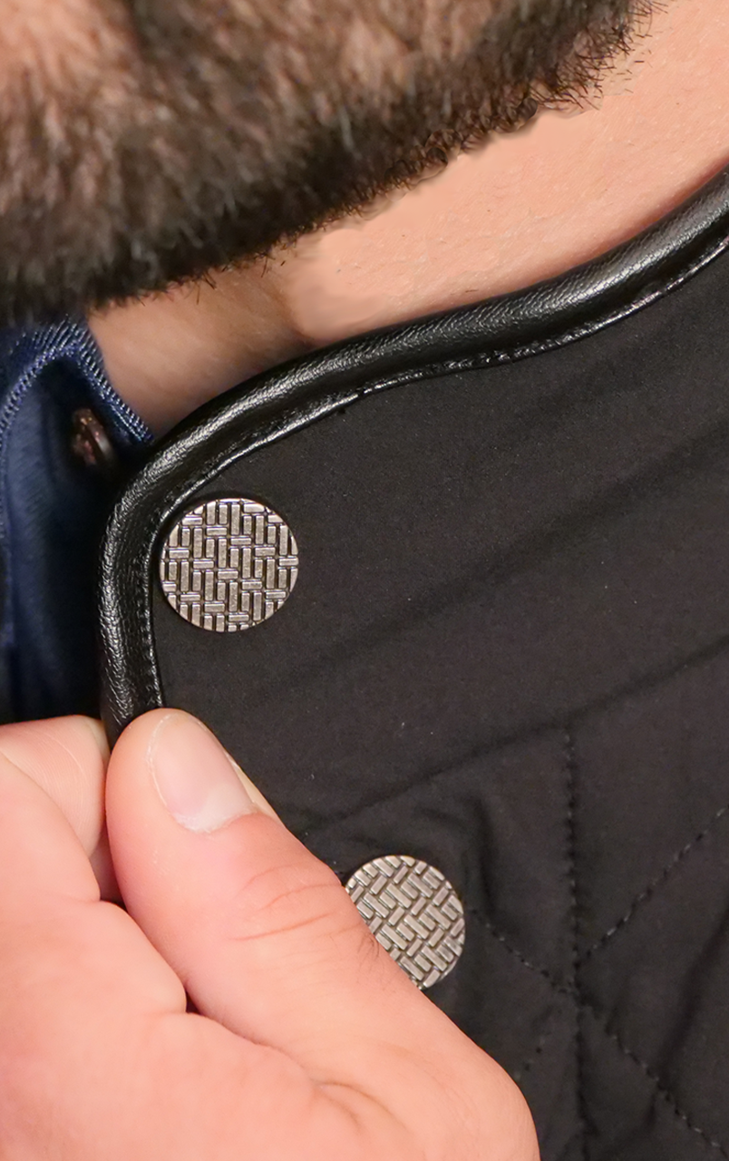 Close-up of a person adjusting the collar of a black quilted jacket with silver woven buttons, showcasing stylish outerwear details.