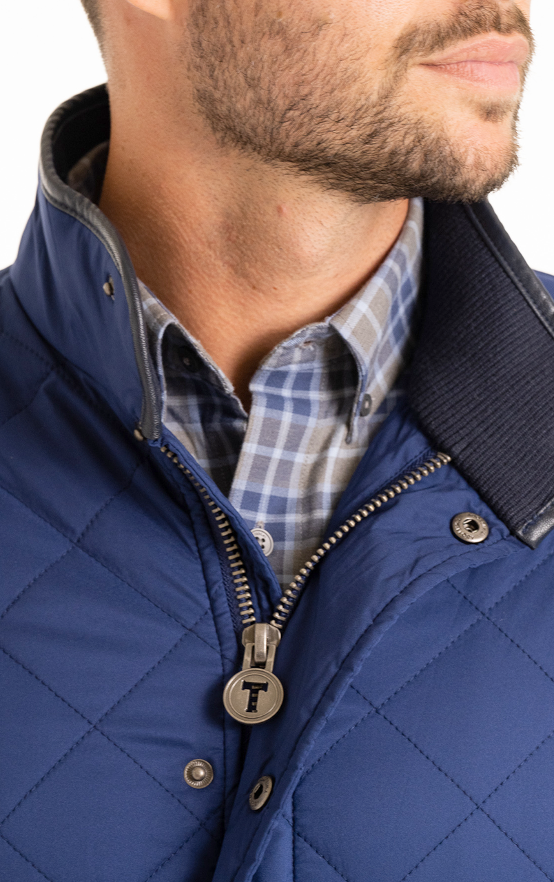 Man wearing a blue quilted jacket with a plaid shirt underneath, focused on the jacket's zipper and collar detail.