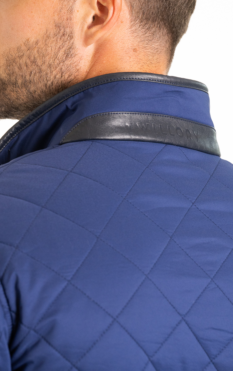 Close-up of a person wearing a quilted blue jacket with a leather collar detailing.
