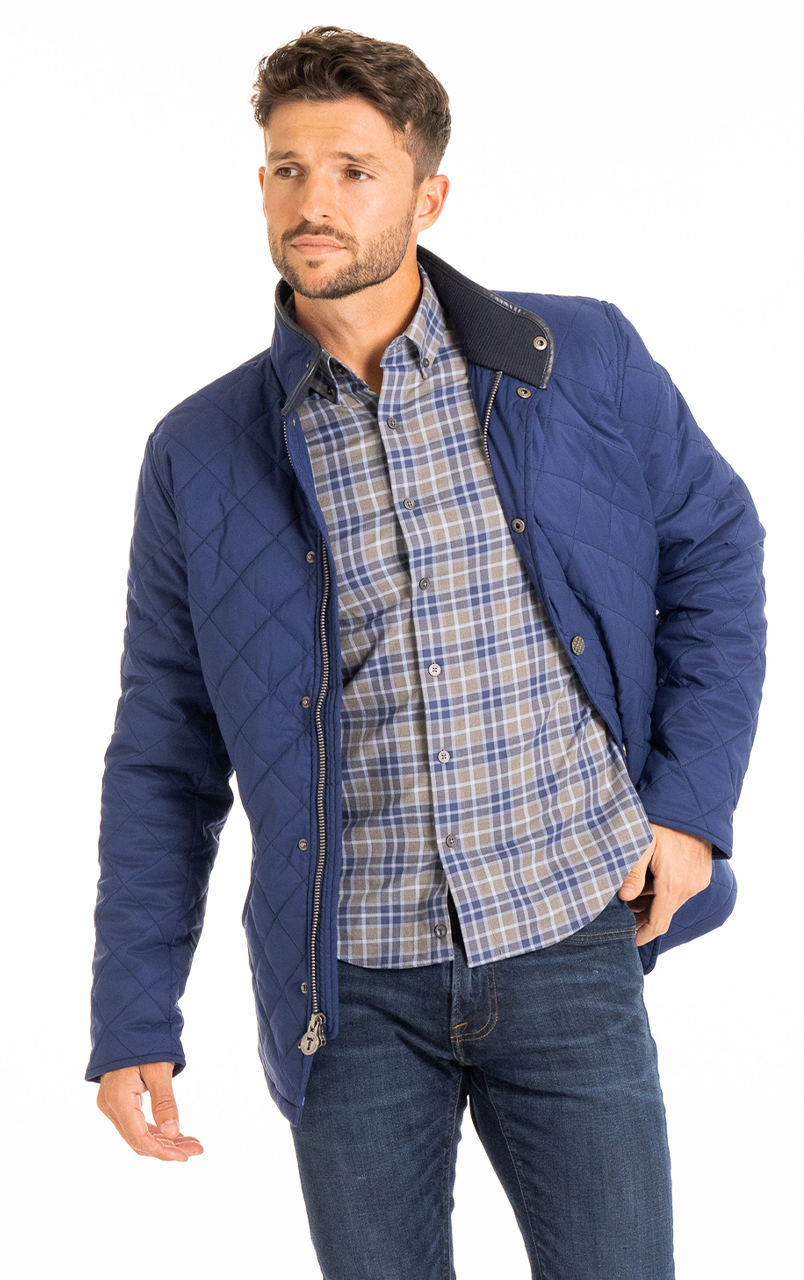 Man wearing a blue quilted jacket over a plaid shirt and jeans.