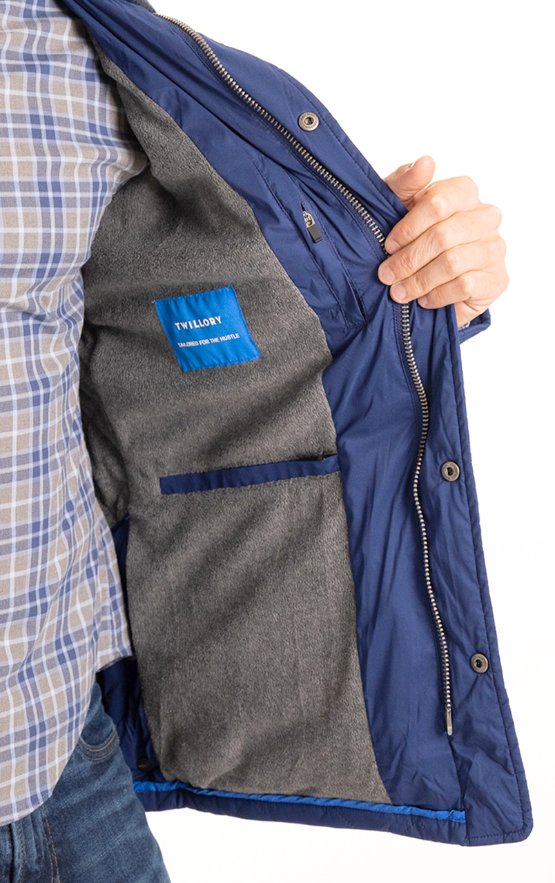 Man wearing open blue jacket with grey lining, displaying Twillory label, and checkered shirt.