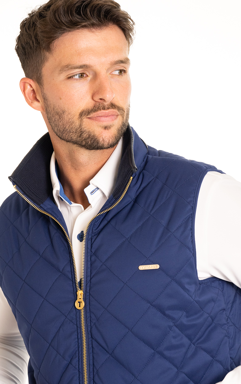 Man wearing a blue quilted vest with a white collared shirt, looking to the side.