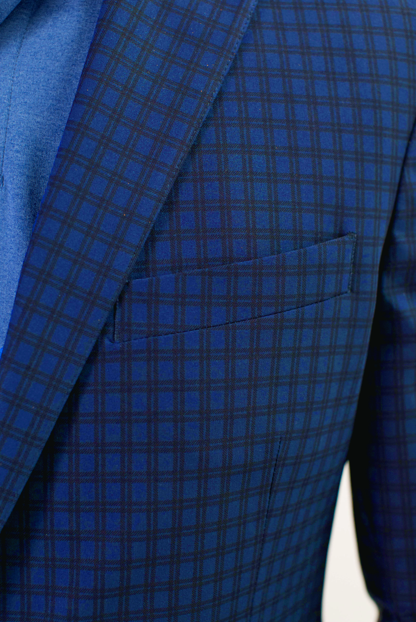 Close-up of the Twillory Performance Blazer // Blue Check, featuring a dark blue check pattern with detailed fabric texture. The lapel, chest pocket, and part of the blue shirt underneath highlight its stylish design.