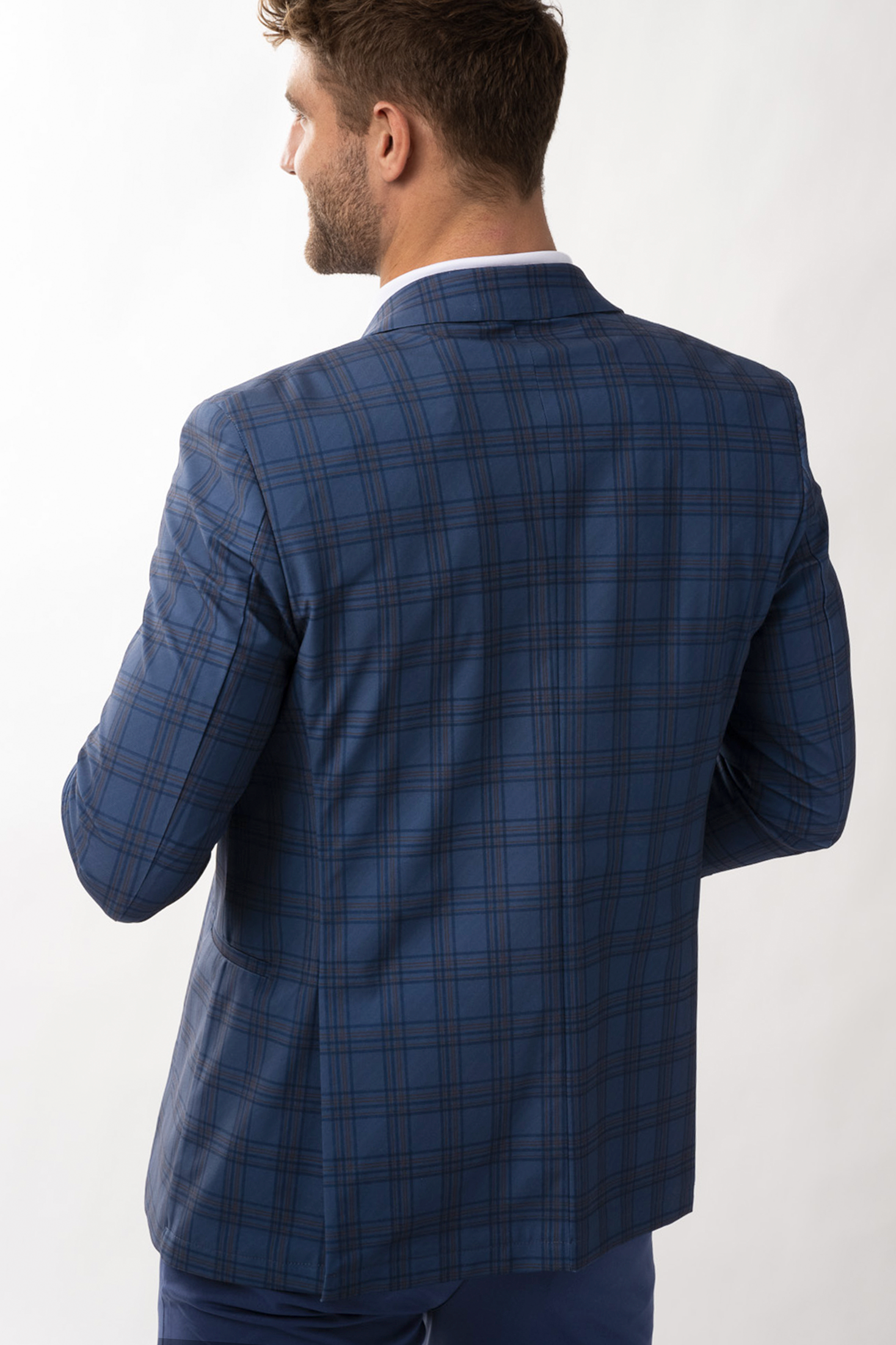 A man with short brown hair, seen from behind against a plain light background, wears the Twillory Performance Blazer // Blue Plaid with thin dark lines. His head is turned slightly right and his left hand rests near his waist.