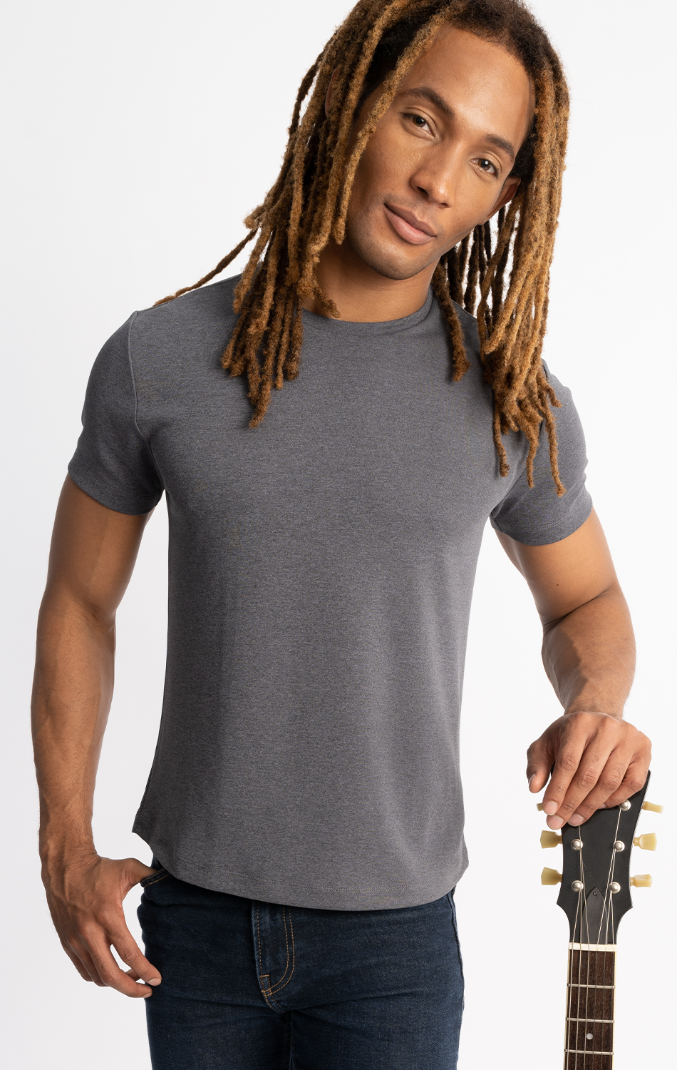 Man with dreadlocks wearing gray t-shirt and jeans, holding a guitar against white background.