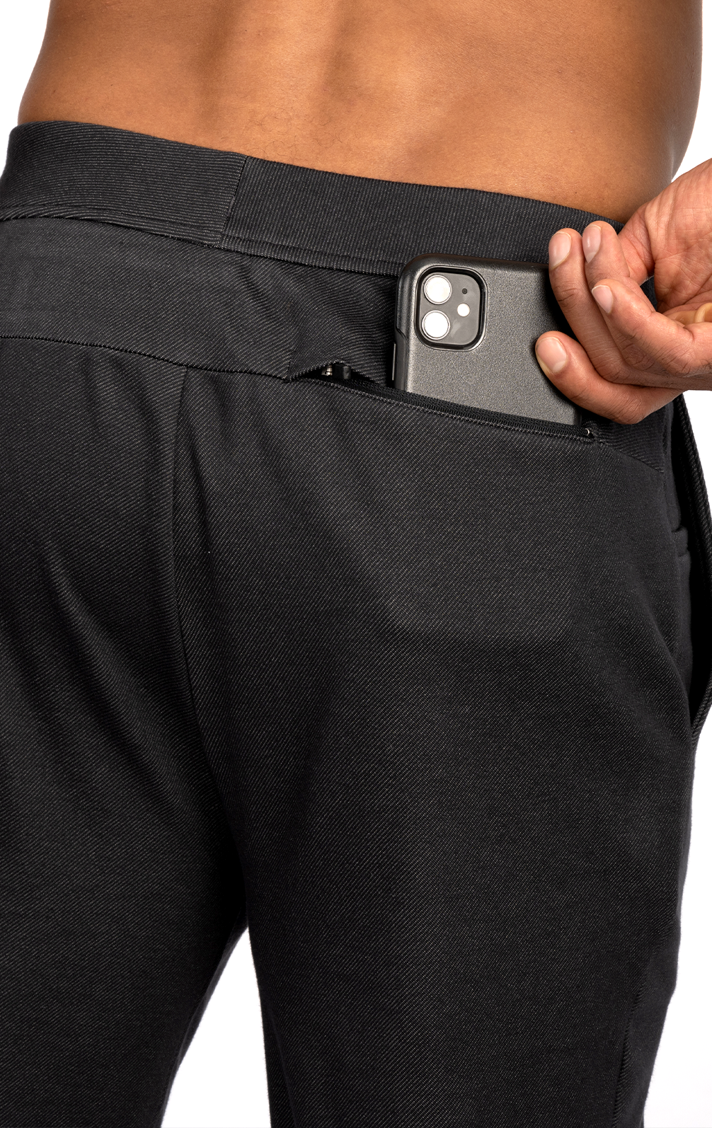 Wearing Twillory’s Athlounger Jogger, a person slips a dual-camera smartphone into the zippered back pocket—the close-up focuses on their hand, the phone, and the jogger’s comfortable fabric at the lower back and waist.