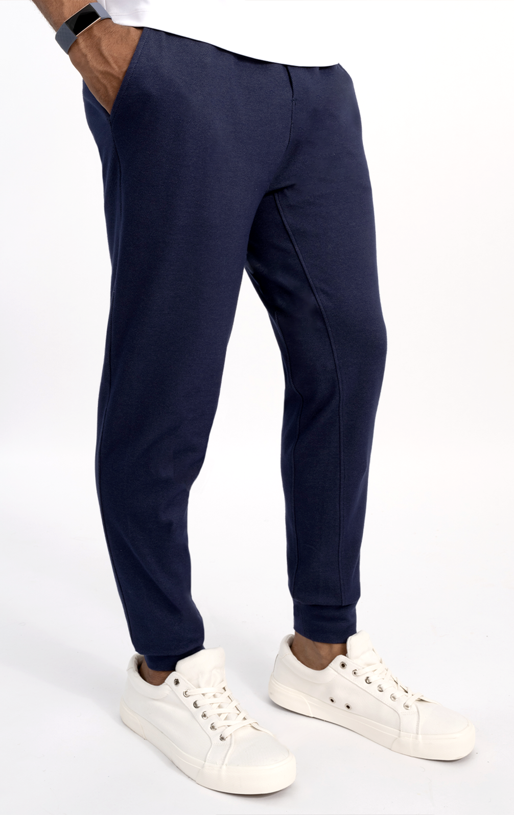 Only the lower body is visible as a person stands against a white background, wearing Twillory Athlounger Joggers in dark blue comfort fabric with a handy side-zip pocket, paired with white sneakers and hands in the pockets.