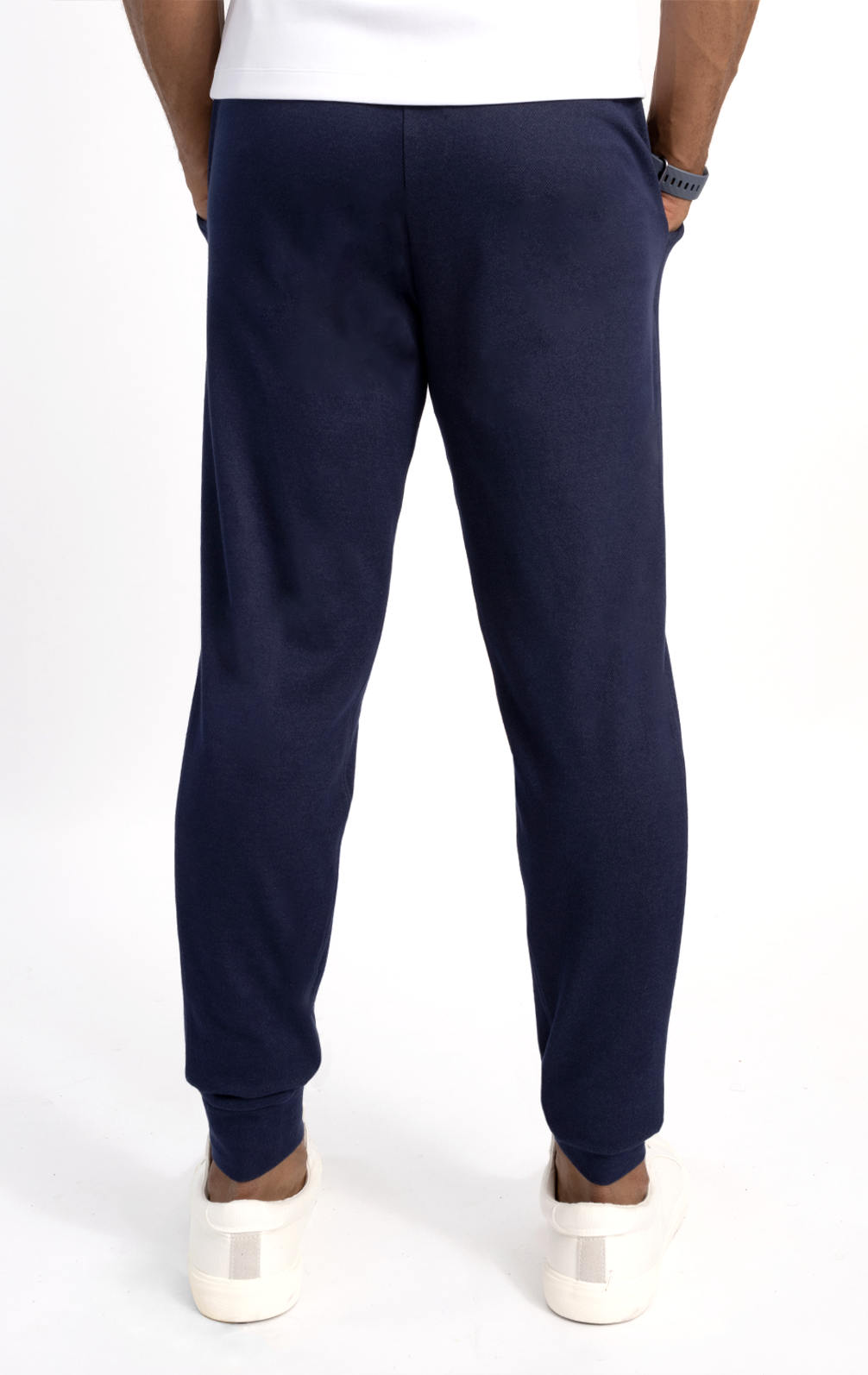 Wearing Twillory's Athlounger Jogger in navy, a person stands shoulders-down with hands in pockets—one with a side-zip—paired with a white tee, dark watch, and white sneakers. The scene is set against a plain white background.