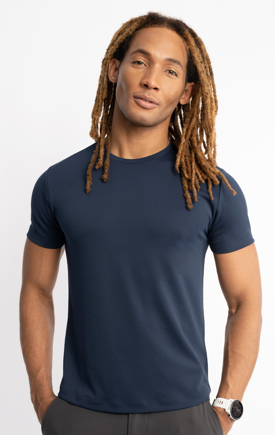 Man wearing a navy blue t-shirt with long dreadlocks smiling confidently against a white background