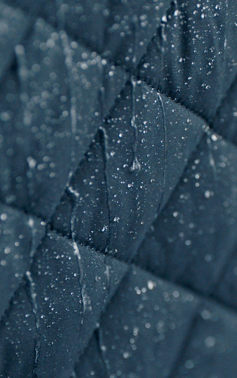 Close-up of dark quilted fabric with visible water droplets, displaying a textured pattern.