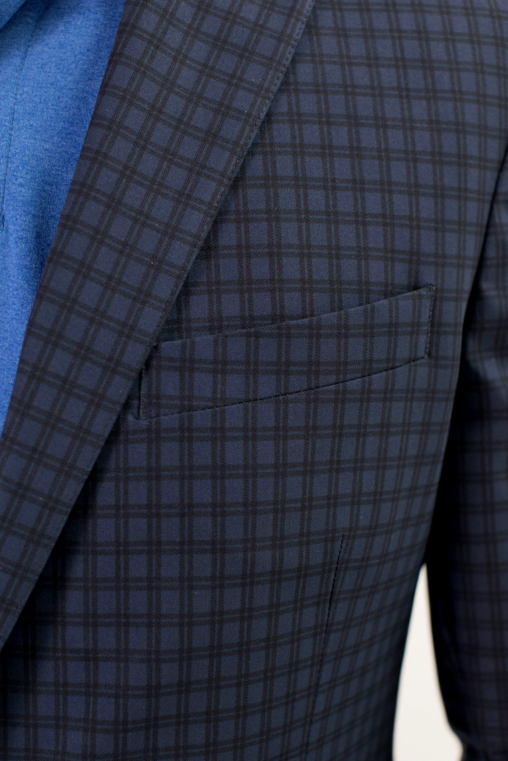 Close-up of a man wearing the Twillory Performance Blazer // Navy Check over a blue shirt. The image highlights the jacket’s breast pocket, lapel, and detailed navy check pattern with its smooth, stretch performance fabric.