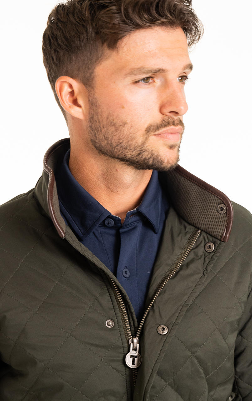 Man wearing a green quilted jacket with a navy blue shirt underneath, looking to the right.
