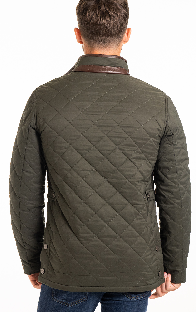 Back view of a man wearing a quilted green jacket with a brown collar and blue jeans.