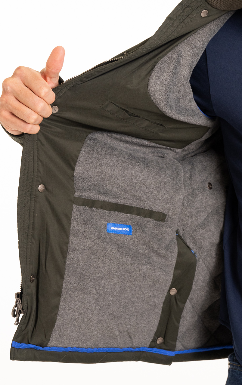 Person showing the inside of a jacket with magnetic hood label, featuring gray lining and button closures, highlighting outerwear design and functionality.