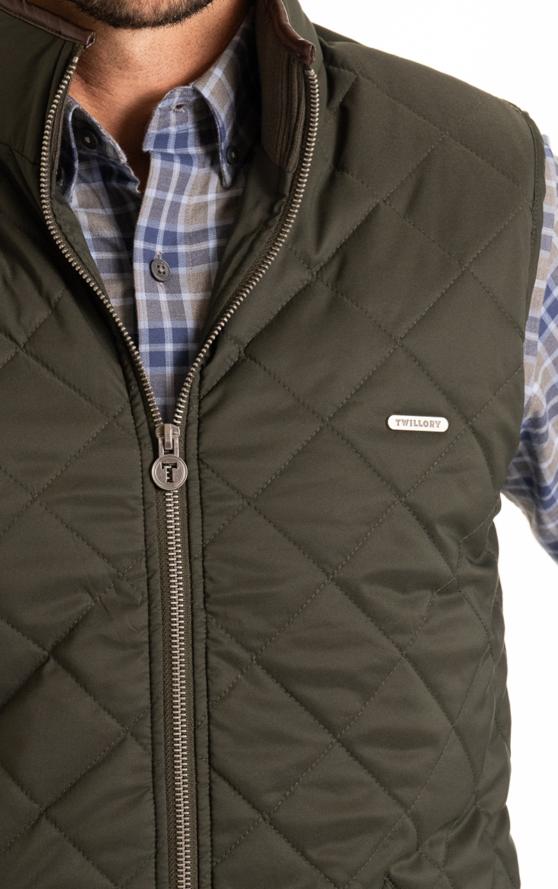 Man wearing a green quilted vest with a plaid button-up shirt underneath.