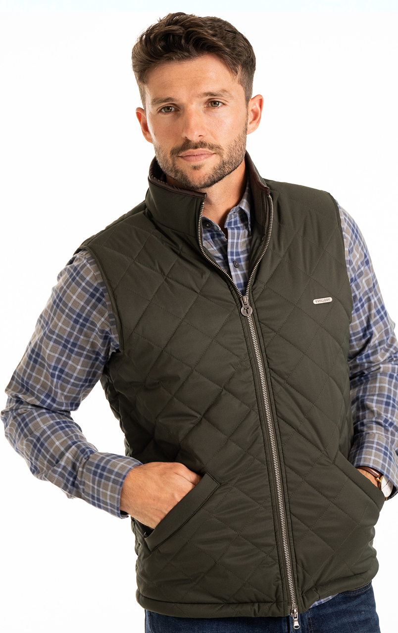 Man wearing a green quilted vest over a blue plaid shirt, posing against a white background.