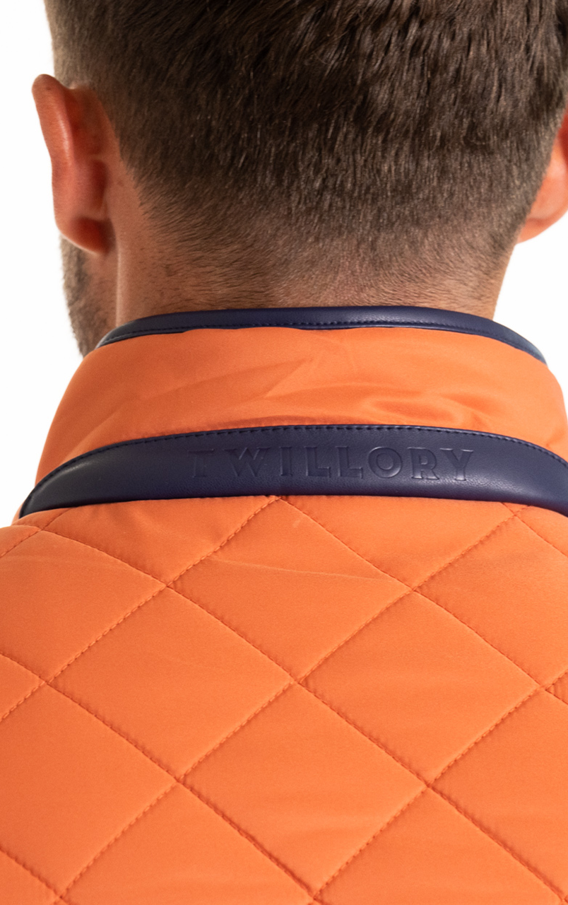 Back view of a man wearing an orange quilted jacket with a navy collar, featuring the brand name Twillory embossed on it.