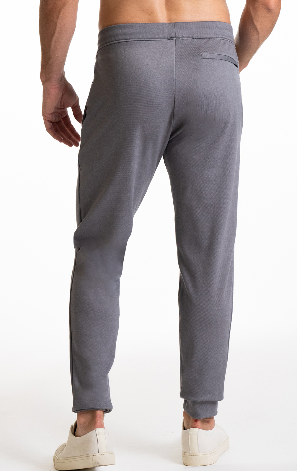 A man faces away from the camera in Twillory Athlounger Jogger pants, featuring a tapered fit and a right-side back pocket. He pairs them with white sneakers, his left arm bent slightly, all set against a plain white background.